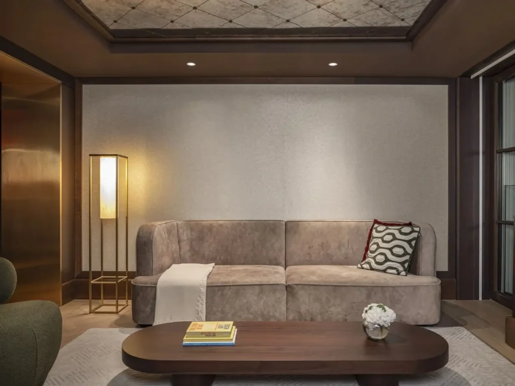 Modernes Familienzimmer mit beigem Ecksofa, geometrischem Kissen, Decke, Holztisch mit Büchern und Vase, Stehlampe und zurückhaltender Deko - ideal als stilvolle Familienunterkunft.